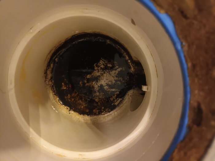 Missfärgad avloppsbotten i badrum med mörkbrun beläggning.