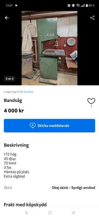 Grön bandsåg från märket Osma, stående i en verkstadsmiljö med en sopkorg och verktygstavla i bakgrunden.