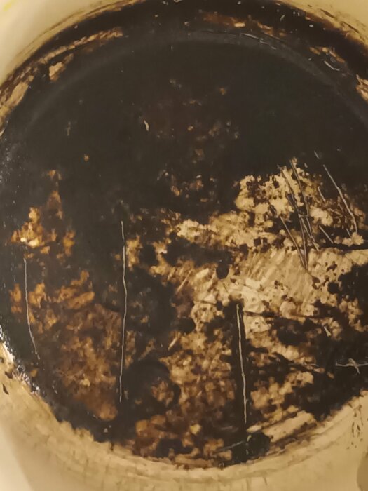 Sprickor och mörka märken i en rund keramisk yta, troligen botten av ett handfat, fotograferade nära för att visa detaljerna.