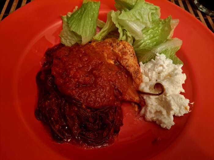 Tallrik med kyckling, nudlar, kryddig tomatröra, sallad och vit kräm.