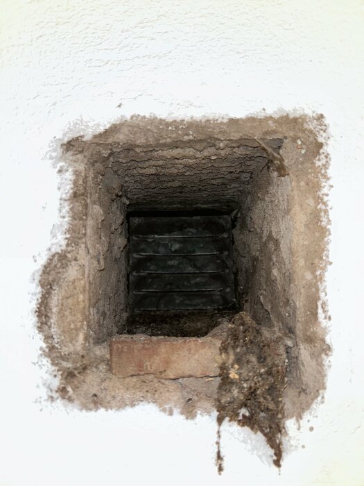 Ventilationshål i betongvägg med synlig lervittring och smuts runt kanterna.
