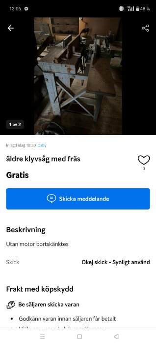 Äldre klyvsåg med fräs visas, placerad i verkstadsmiljö med träbord och metallställning. Ljuset är dämpat och sågen är utan motor.