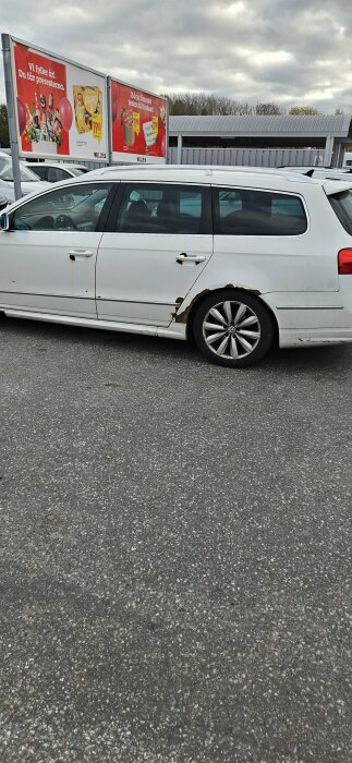 Bilmodell VW Passat från 2010 med rostskador på dörr och hjulhus, parkerad vid en skylt i ett bilmörkt område.