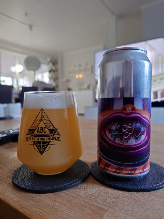 Ett glas med öl från Apex Brewing Company och en matchande ölburk, placerade på ett bord i ett vardagsrum.