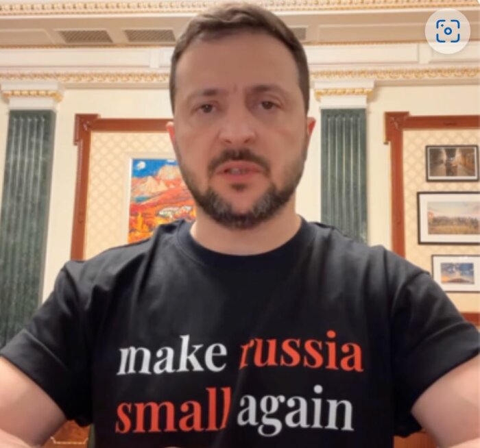 En person i svart t-shirt med texten "make russia small again" står i ett rum med inramade bilder på väggen.