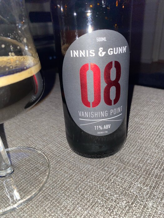 En flaska Innis & Gunn Vanishing Point 08 imperial stout 11% ABV, med ett glas öl bredvid, på ett bord.
