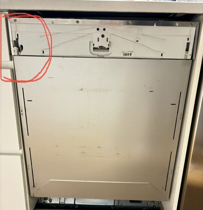 Trasigt plastfäste på luckan till en integrerad Miele diskmaskin, med röd markering runt det skadade området.