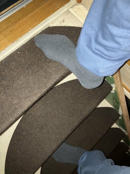 Person går ner för en smal, mörkbrun trappa med grå strumpor.