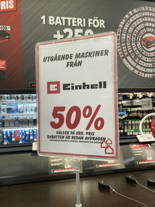 Skylt i en butik som annonserar 50% rabatt på utgående maskiner från ett specifikt märke. Rabatt gäller på ordinarie priser, exkluderar startkit, batterier och laddare.