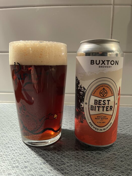 Ett glas med engelsk bitteröl bredvid en burk med etiketten "Buxton Brewery Best Bitter 4.2% ABV".