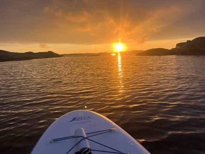 Solnedgång över ett stilla hav, sedd från en surfbräda. Strålar från solen reflekteras i vattnet.