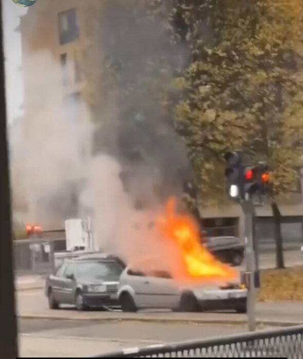 Bilbrand på gata, bogserande bil brinner under motorhuven medan den andra bilen står framför; båda bilarna är icke-elbilar.