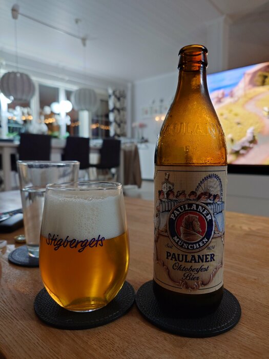 En flaska Paulaner Oktoberfest Bier och ett glas öl med skum, stående på ett bord i ett modernt vardagsrum.