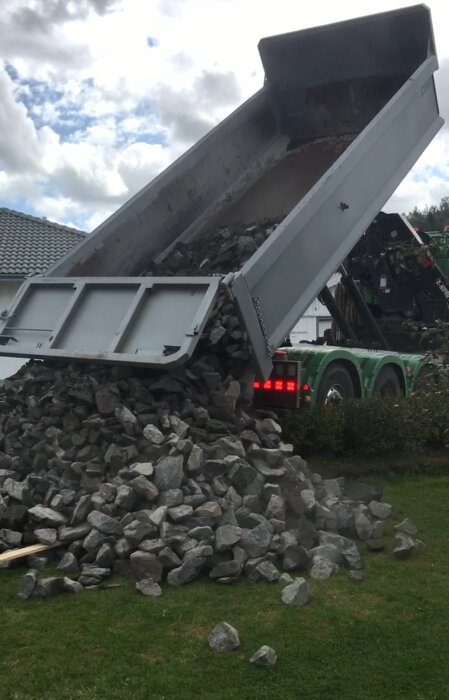 Lastbil tippas last av stenblock på gräsmatta under byggprojekt.