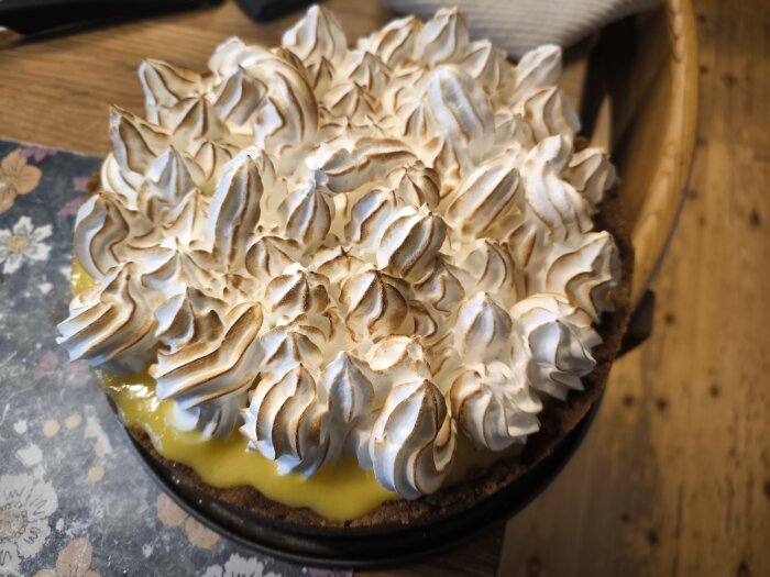 Mango och lime cheesecake med italiensk maräng spritsad oregelbundet ovanpå, fotograferad på ett träbord.