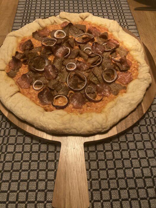 Surdegspizza med ostkant, toppad med kött och lök, ligger på en träspatel.