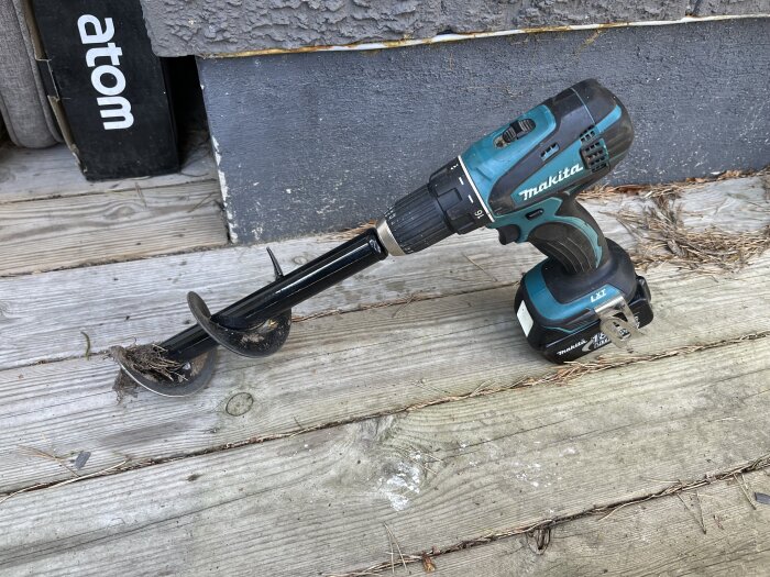 En Makita batteridriven borrmaskin med jordborr på trädäck, används för trädgårdsarbeten och plantering.