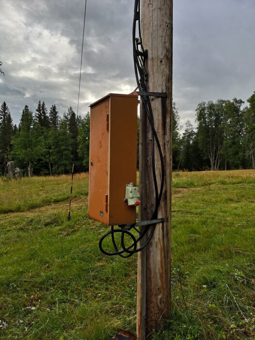 Elskåp fäst vid en trästolpe på ett fält, med elledningar som går in i skåpet.