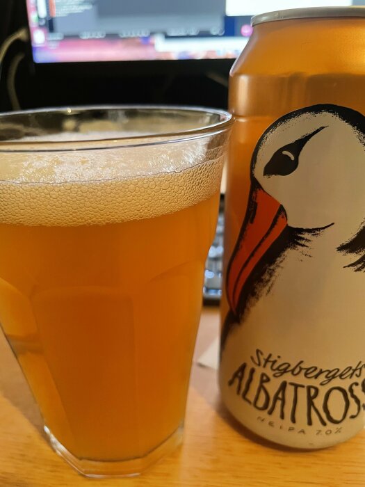 En ölburk märkt "Stigbergets Albatross" bredvid ett glas med skummande öl framför en datorskärm.