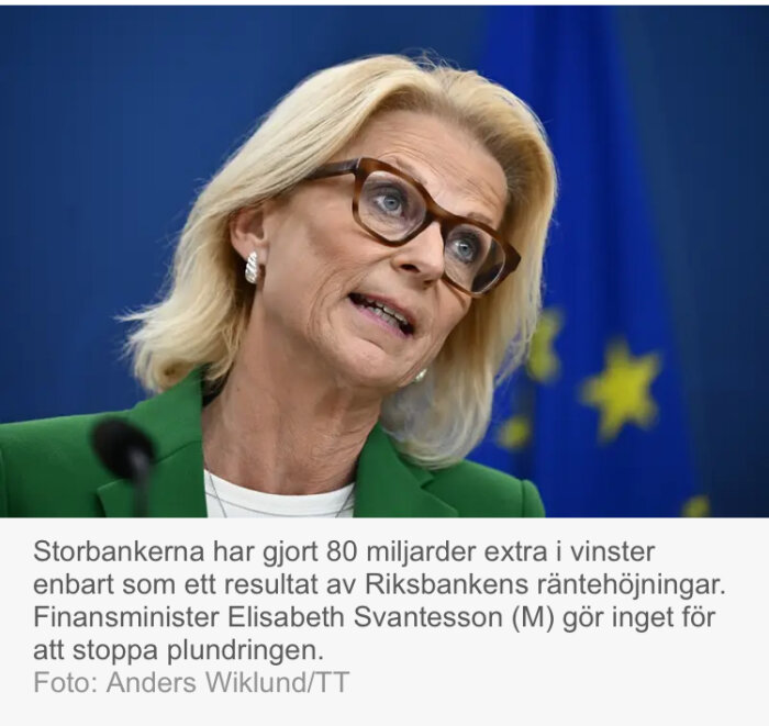 Kvinna med glasögon talar framför en blå bakgrund med EU-stjärnor.