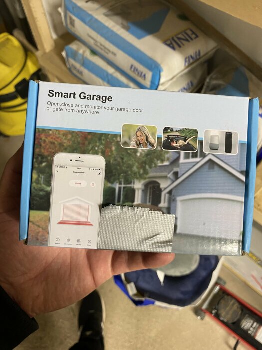 Förpackning för smart garageöppnare ses i handen, med text "Smart Garage" och bilder av garage och smartphoneapp på framsidan.