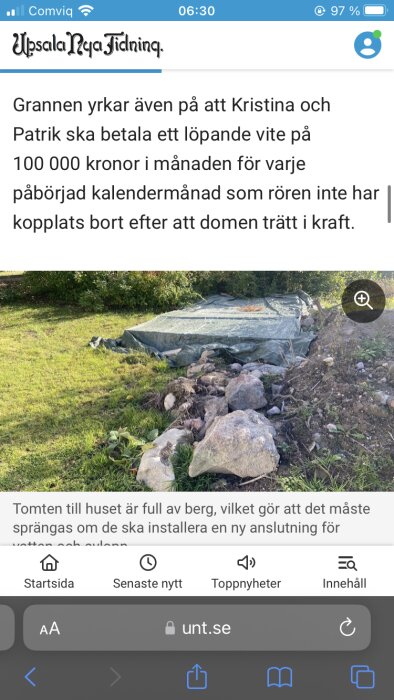 Bild på en tomt med flera stora stenar och jordhögar, täckt med en presenning. I bakgrunden syns träd och buskar.