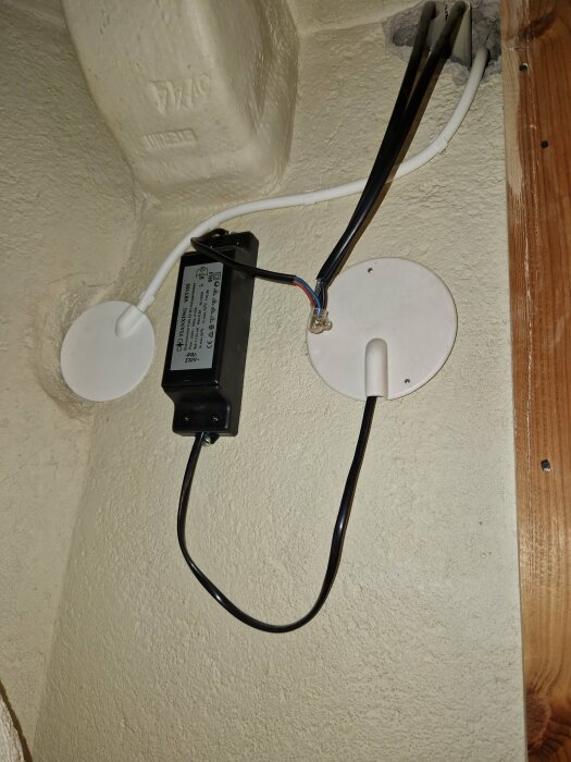 Elektrisk installation i ett kopplingsutrymme med svart apparatkabel fäst vid en svart enhet och vita kabelhöljen på väggen.