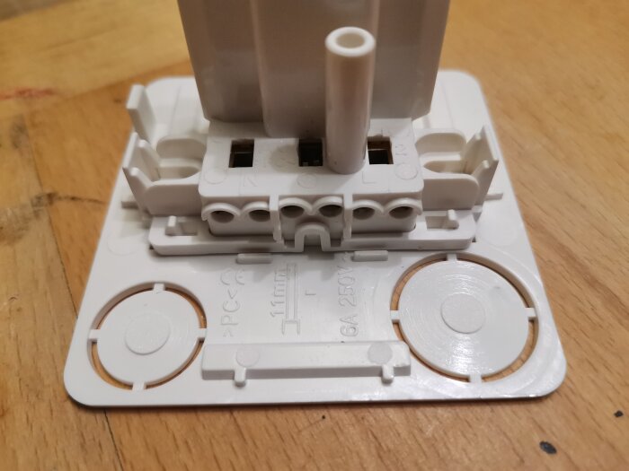 Närbild på ett DCL-uttag med flera kabelingångar för fas, nolla och jord på en träyta. Uttaget har märkning för 250V och 6A.
