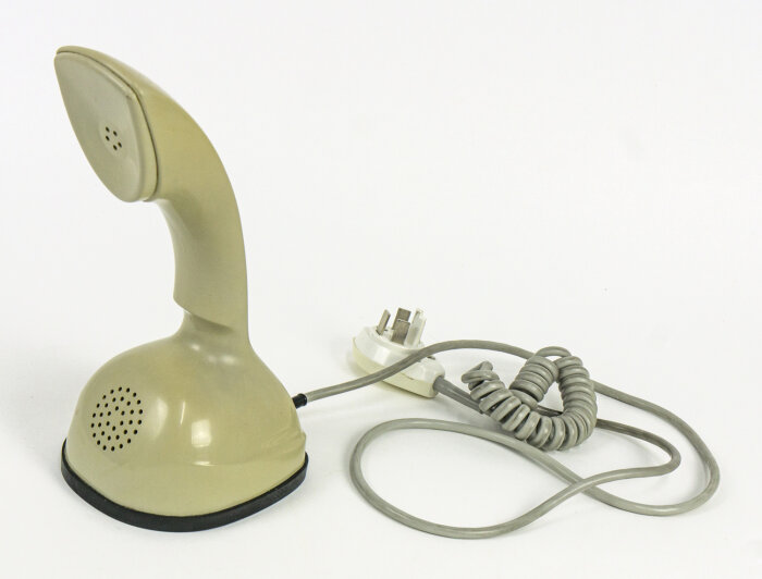 Retro Kobra-telefon i beige med spiralformad sladd och strömplugg, känd för att sakna inbyggd ringklocka.