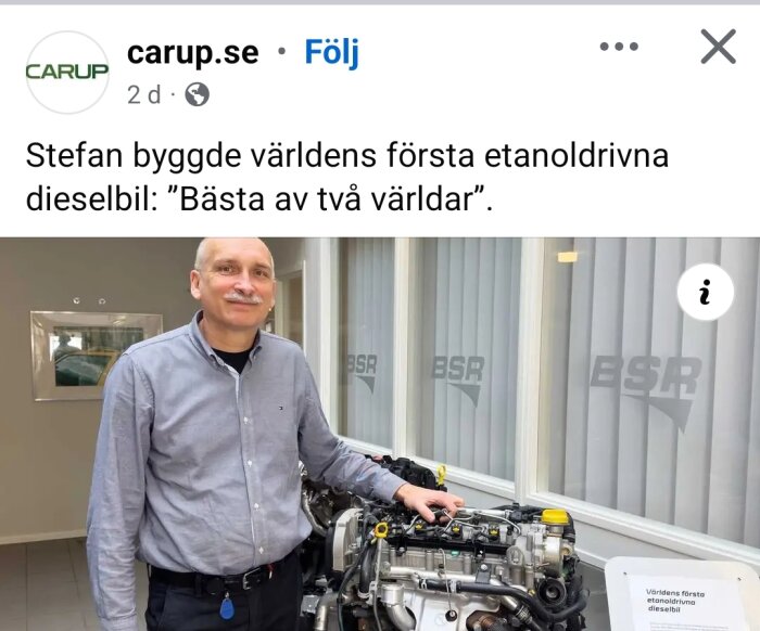 Man vid motor av världens första etanoldrivna dieselbil, leende i silvergrå skjorta, med skylt om "bästa av två världar" i bakgrunden.