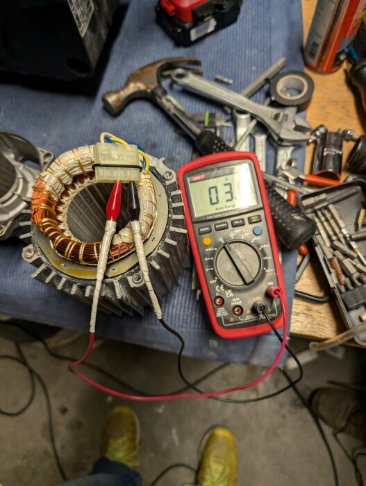 En isärplockad enfasmotor med mätkablar anslutna och en multimeter som visar resistansen 3,7 ohm, omgiven av verktyg på en bänk.