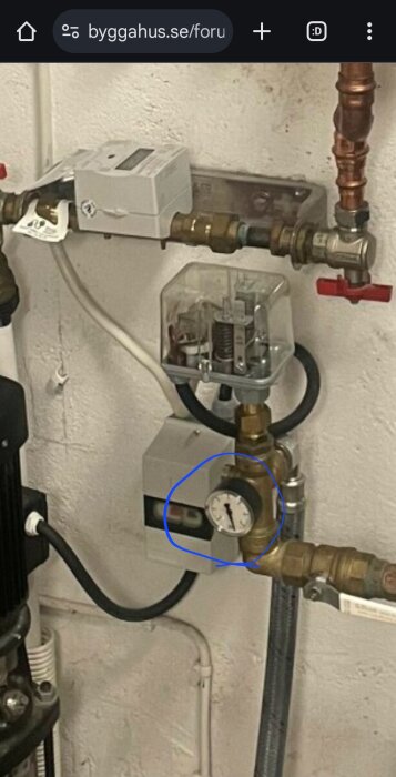 Manometer och tryckströmbrytare i ett vattenpumpsystem, omringade av rörkopplingar och ventiler.