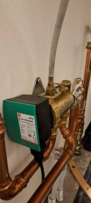 Pumpinstallation med grönt lock och kopparrör i byggnad.