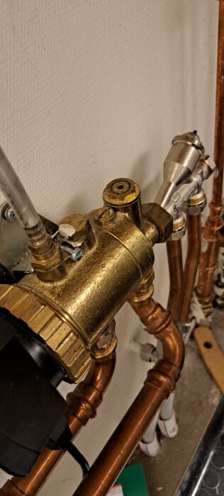 VVS-armatur med kopparrör och metallventiler utan synlig skruv bakom grönt lock.
