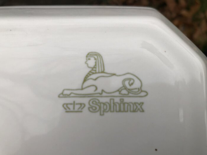 Närbild på tvättställsmärkningen "Sphinx" med en liggande sfinx och krona.