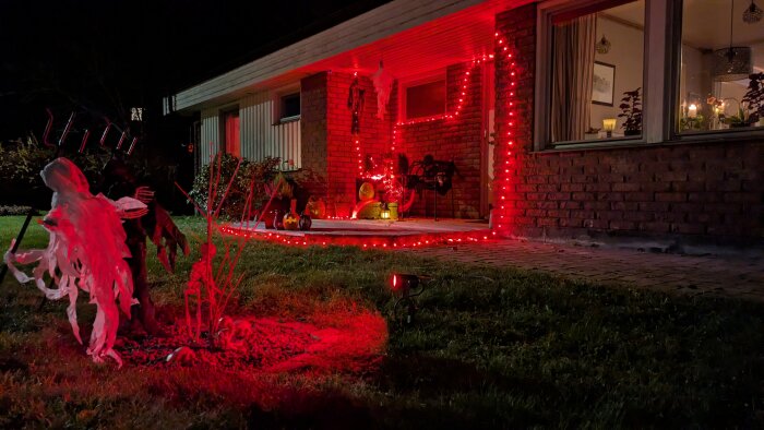 Halloween-dekorationer med spöken och röda ljus på en veranda. Pumpor och andra dekorationer syns på marken.