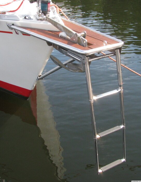 Rostfritt stålpeke på segelbåt med trädäck och stege över vatten.