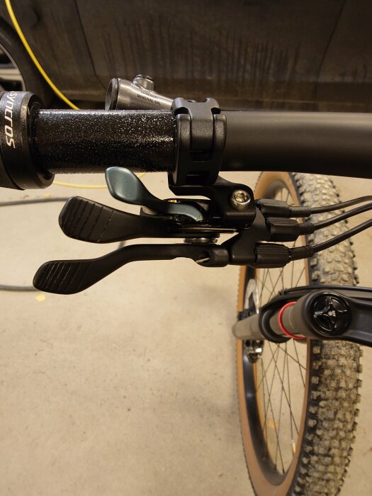 Närbild av cykelstyre med monterad dropper-post-kontroll, nysatt wire och två insexnycklar. Cykelns framdäck och ram syns i bakgrunden.