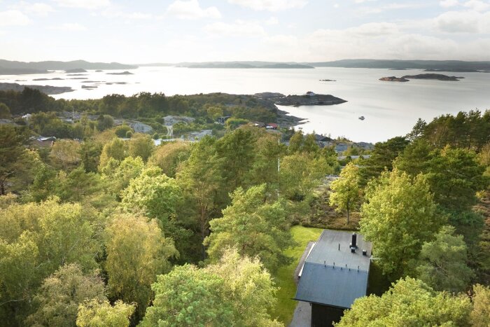 Flygfoto över Tjörn med utsikt över skog och hav, ett modernt hus syns delvis i förgrunden.