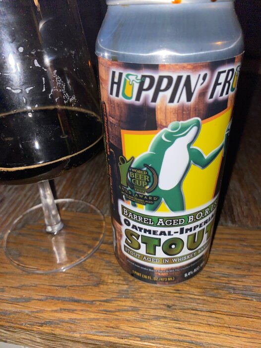 Ölburk av märket Hoppin' Frog Barrel Aged B.O.R.I.S. Oatmeal-Imperial Stout och ett glas fyllt med samma stout på ett träbord.