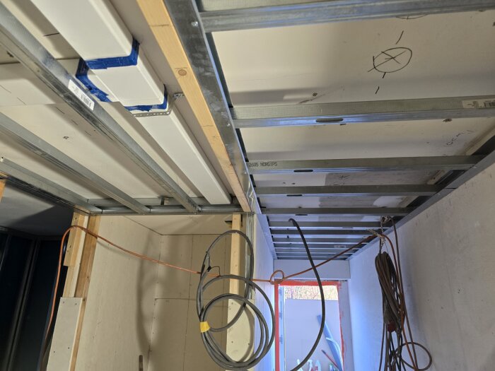 Byggprojekt pågår med arbete på takets ventilation och elinstallationer, exponerade rör och kablar syns mot ett öppet tak i ett rum.