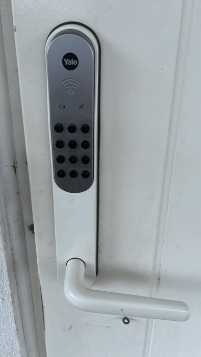 Digitalt Yale kodlås installerat på vit ytterdörr med nummerknappar och dörrhandtag.