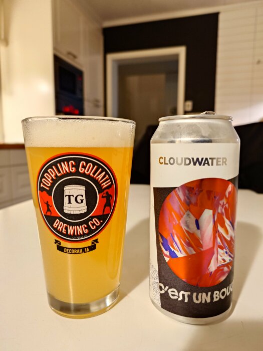 Ett glas öl från Toppling Goliath och en Cloudwater-burk med färgglad etikett på ett bord i ett modernt kök.