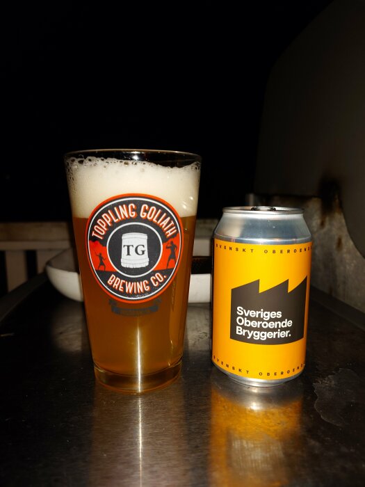 Ett glas öl från Toppling Goliath Brewing Co och en ölburk från Sveriges Oberoende Bryggerier på ett metallbord.