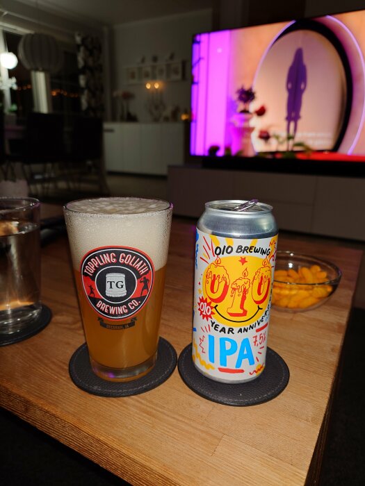 En burk O/O Brewing 10-års jubileums IPA och ett glas öl på ett bord framför en TV.