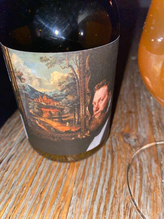 Flaska med etikett från Fader Rödskägg Vreta kloster bryggeri och ett glas öl på ett träbord.