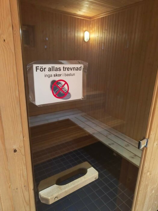 Skylt på bastudörr med texten "För allas trevnad inga skor i bastun" och en bild av skor med överkryssad röd cirkel.