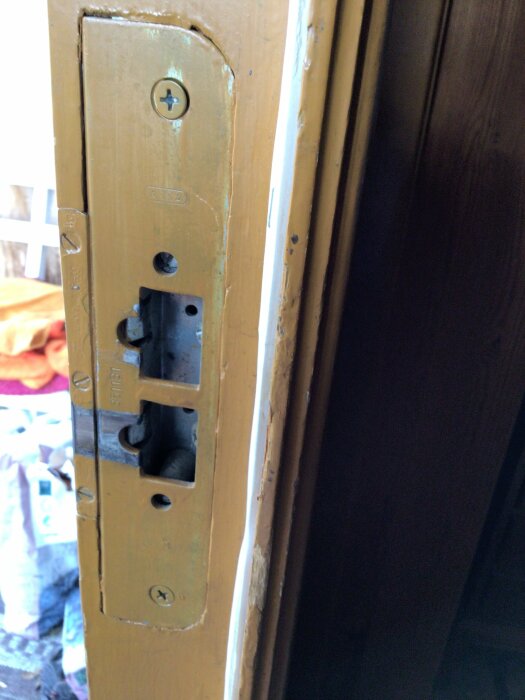 Närbild av en gulnad dörr med låsuttag utan handtag installerat, omgiven av verktyg och material i bakgrunden.