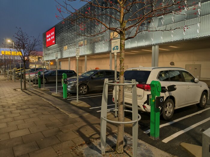 Elbilar vid laddstation utanför Ikea Umeå, flera parkeringsplatser synliga på en dimmig dag.