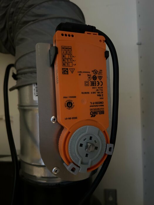 Orange elektrisk motor ansluten till ett ventilationssystem med synliga kablar, inklusive en vit kabel.